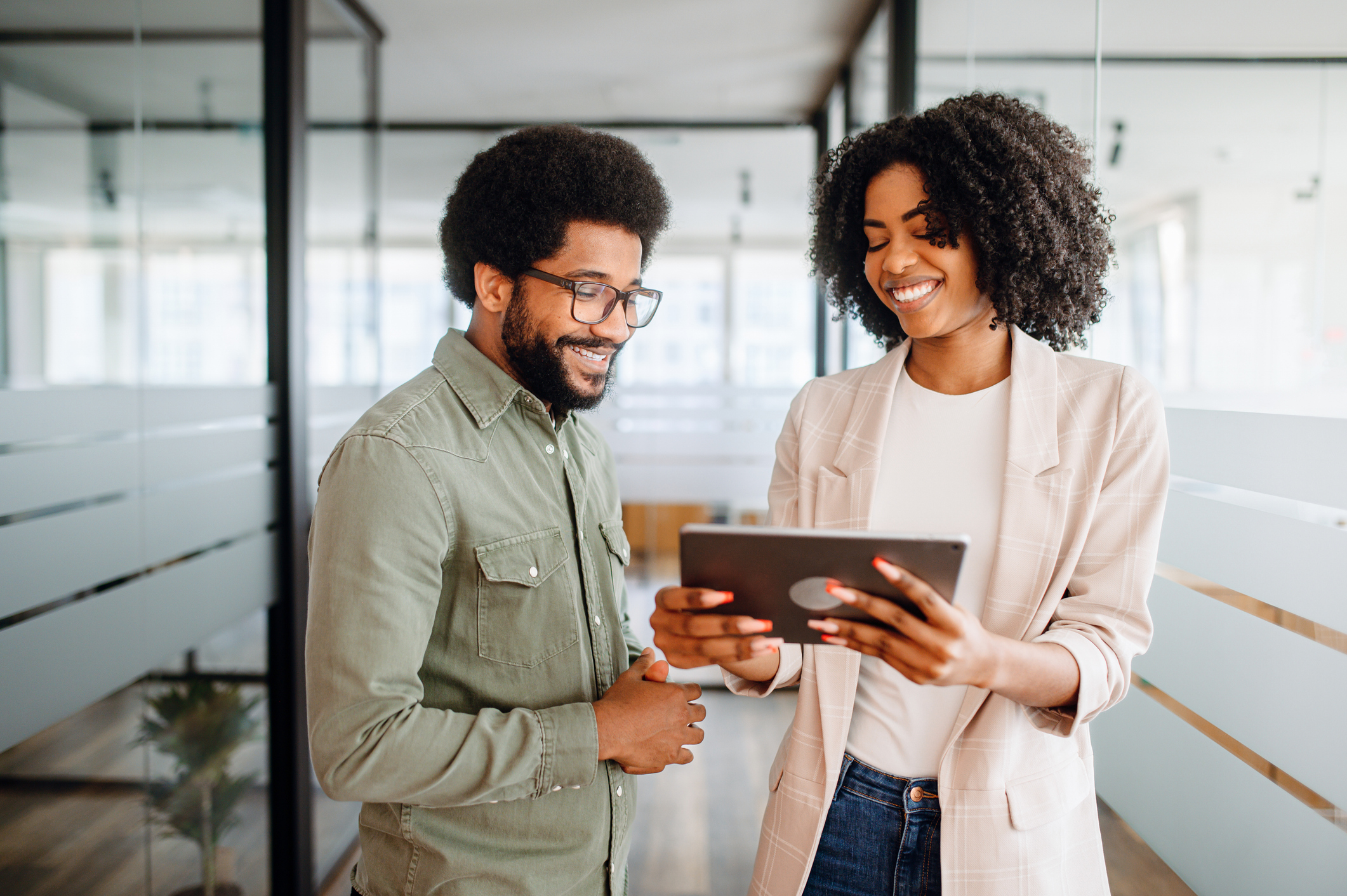 Two cheerful colleagues are sharing a tablet screen, the woman pointing at the screen, a man watching with interest, collaborative and friendly work atmosphere. Team interaction and knowledge exchange