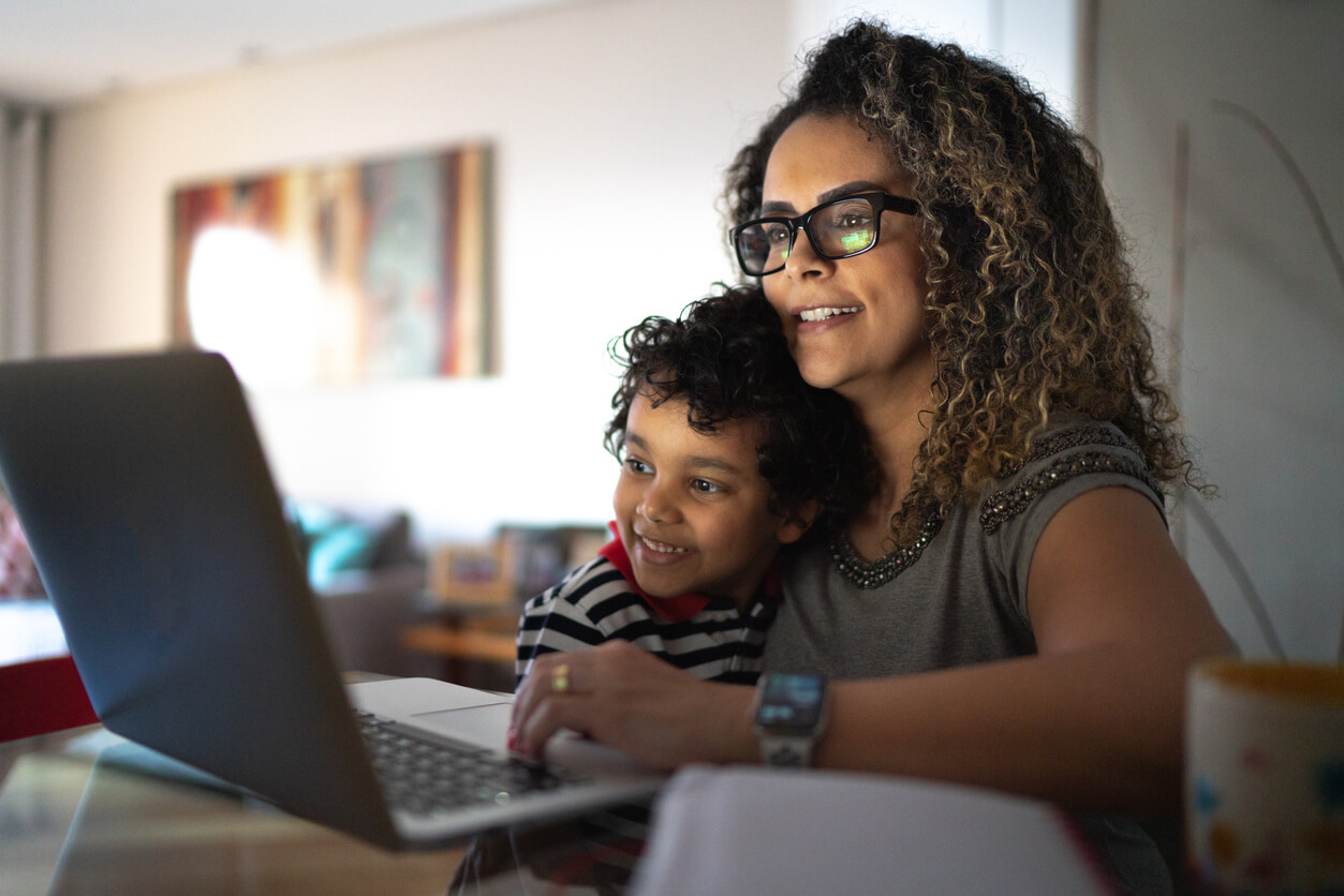 A mother and her child are sitting in front of a laptop, looking at its screen